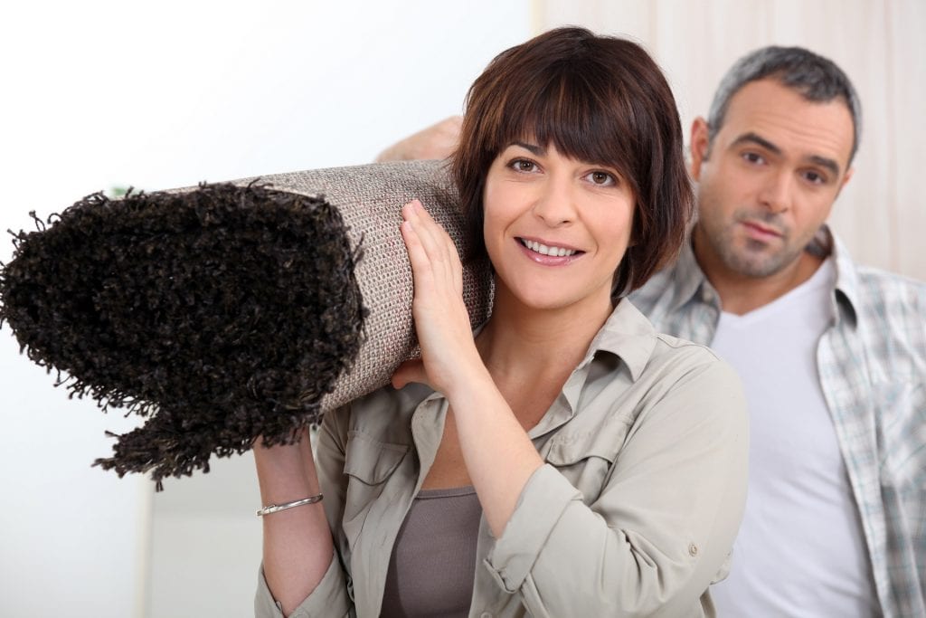 A woman and a man carrying a rug